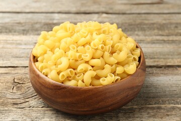 Raw horns pasta in bowl on wooden table, closeup