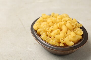 Raw horns pasta in bowl on gray textured table, closeup. Space for text