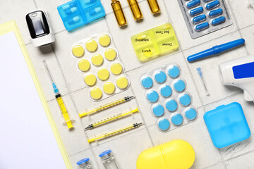 Medical supplies with insulin syringe and pills on white tile background. Top view