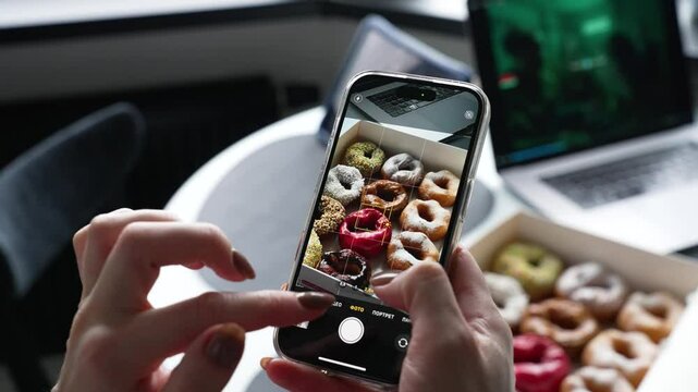 Close up of mobile phone, girl taking picture of box of sweet donuts