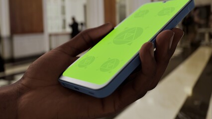 GREEN SCREEN CHROMA KEY Person holding a smartphone in a luxurious lobby with elegant architecture, marble flooring, and blurred background activity