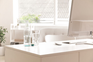 Bottle of water with glass on desk in light office