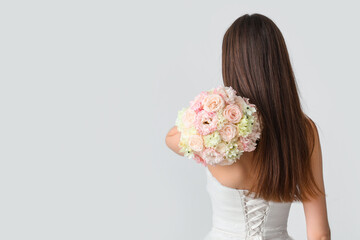 Beautiful bride with wedding bouquet on light  background, back view