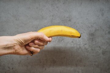 Hand Holding Banana Like a Gun Against Concrete Wall