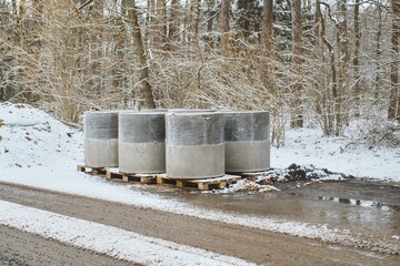 Concrete Sewer Pipes Wrapped in Plastic on Snowy Construction Site in Forest