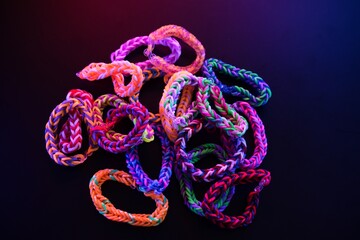 Pile of Colorful Loom Band Bracelets Glowing in Blacklight – Bright Neon Rubber Accessories on Dark Surface