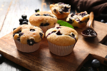 Wooden tray with tasty blueberry muffins on black wooden background, closeup