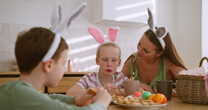 A woman kisses her child daughter on the cheek during a tea party with cookies Easter at home