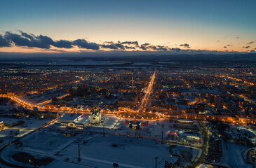 Obraz premium Urban landscape illuminated by evening lights showcasing Yuzhno-Sakhalinsk city at dusk in cold winter conditions.