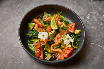 Colorful salad with smoked salmon, fresh avocado, ripe tomatoes, mixed greens, sesame seeds, decorative flowers, healthy lunch concept