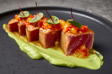 Elegant seared tuna with vibrant salsa, avocado purée, and fresh greens plated on black dish, gourmet cuisine presentation concept
