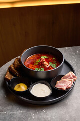 Traditional Ukrainian borscht soup with sourdough bread mustard sour cream and bacon on rustic table culinary presentation concept