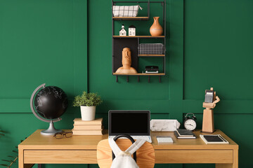 Workspace with school supplies, laptop and backpack near green wall