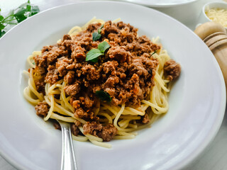 White plate with spaghetti with bolognese sauce and seasonings