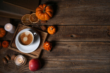 Burning candles with pumpkins, apple, dried orange, books and cup of coffee on wooden table