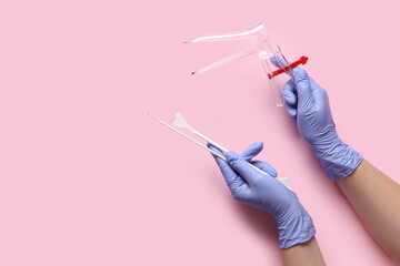 Doctor's hands with gynecological speculum and pap smear test tools on pink background