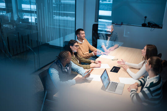 A diverse team of young professionals collaborates in a modern office conference room. Businesspeople discuss strategy, technology, and planning, using laptops to develop an innovative e-commerce