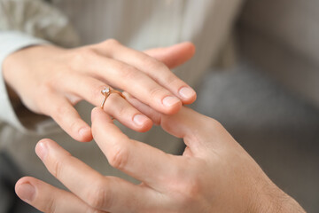Young man putting engagement ring on his girlfriend's finger at home, closeup