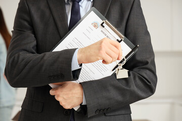 Real estate agent with house rental agreement and key in kitchen, closeup