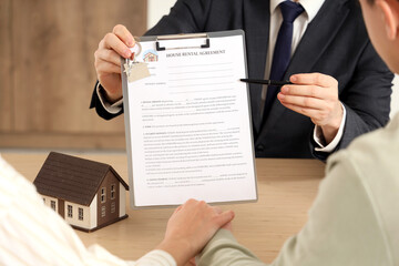 Real estate agent with house rental agreement and couple at table in kitchen, closeup
