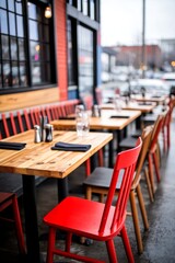 Empty outdoor restaurant tables, red chairs, colorful building, city street in background