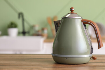 Modern green electric kettle on wooden table in kitchen