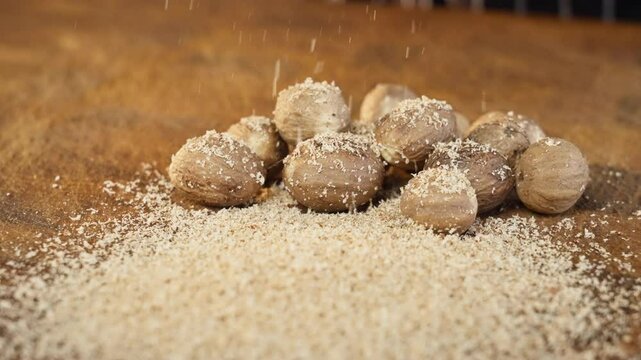 Grating grate nutmeg on a wooden cutting board. Close up, slow motion 50fps. Selective focus.
