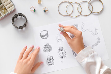 Female jewelry designer with ring and drawings on table in workshop, top view