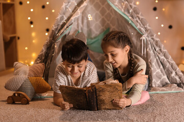 Cute children reading adventure book in play tent at night © Pixel-Shot