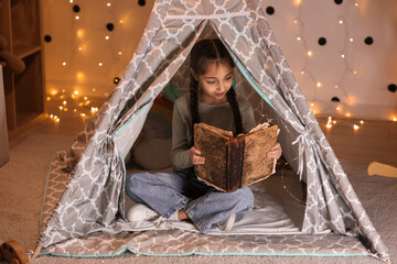 Cute girl reading adventure book in play tent at night