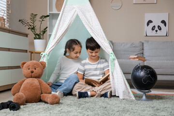 Cute children reading adventure book in play tent at home