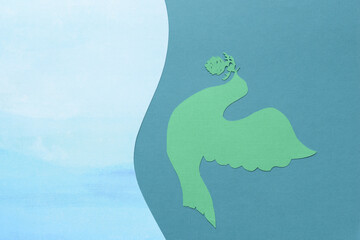 machine-cut dingbat of a bird with a cone flying sideways on green and blue paper with wavy edge