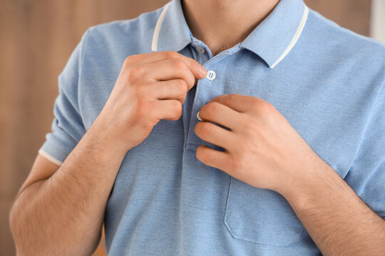 Young man buttoning up blue polo shirt at home, closeup - Powered by Adobe