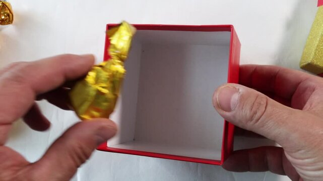 Close-up of a man's hand putting gift candies wrapped in yellow and other colored foil. Candies in hands, top view.