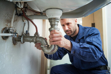Plumber fixing a leaking pipe under the sink in a residential bathroom during the daytime