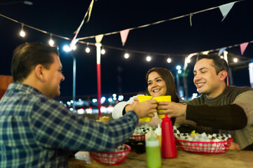 Friends dining outdoors, clinking glasses near illuminated food truck, laughing and celebrating nighttime camaraderie