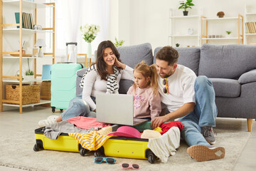 Happy tourist family online choosing trip, booking tickets flight, parents and child at home ready for travelling in bright summer trip holiday beach, packing luggage bag for vacation travel