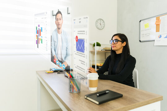 Businesswoman wearing augmented reality glasses attending a virtual meeting and checking emails in a modern office
