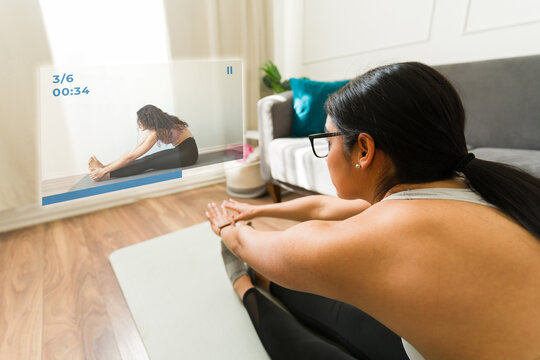 Latin woman wearing augmented reality glasses and practicing yoga at home by following an online class