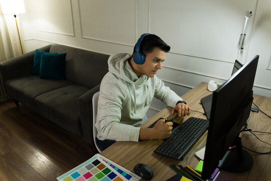Male graphic designer wearing headphones, working on a digital project at home, using a tablet and computer, with design tools nearby