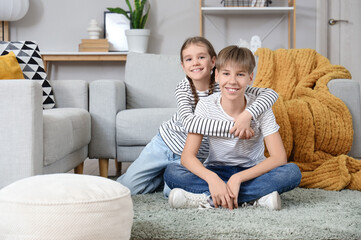 Cute girl hugging her brother on carpet at home