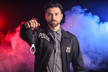 Male police officer with handcuffs in smoke on black background