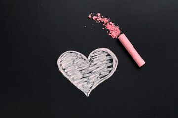Pink chalk with crushed pigment and drawn heart on blackboard