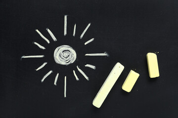 Yellow chalks with drawn sun on blackboard