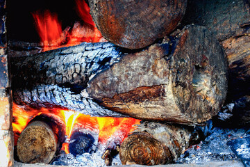 A close-up of burning firewood in a traditional stove. The logs are charred and glowing with intense orange flames, creating a warm and rustic scene. Xinpu Township, Taiwan.