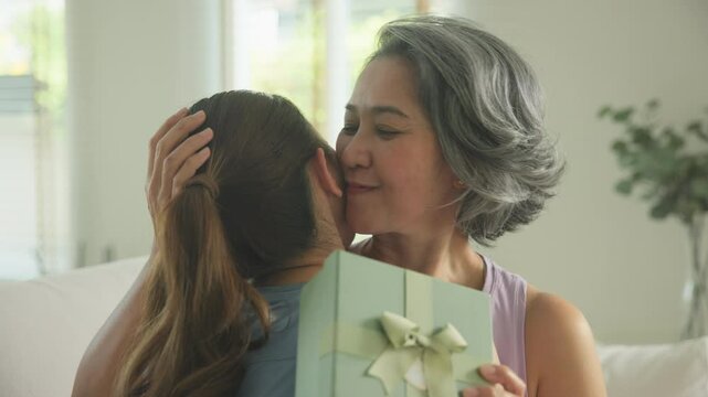 May Mother's day young adult child arm around cuddle hug give gift box to mature middle age old mum. Love kiss care mom asia elder people sit at home sofa happy smile enjoy family good time aging life