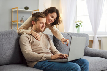 Happy family, young spouses, smiling couple in love using computer laptop together at home, talking...