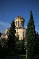 A magnificent church with a golden dome stands tall against a deep blue sky, surrounded by lush green cypress trees. The grand architecture and intricate details reflect historical and religious.
