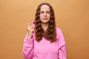 A woman with long, wavy hair is raising her index finger with a thoughtful expression while wearing...