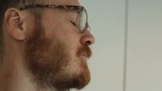 A man in glasses with a red beard chews food. Close-up. Side view